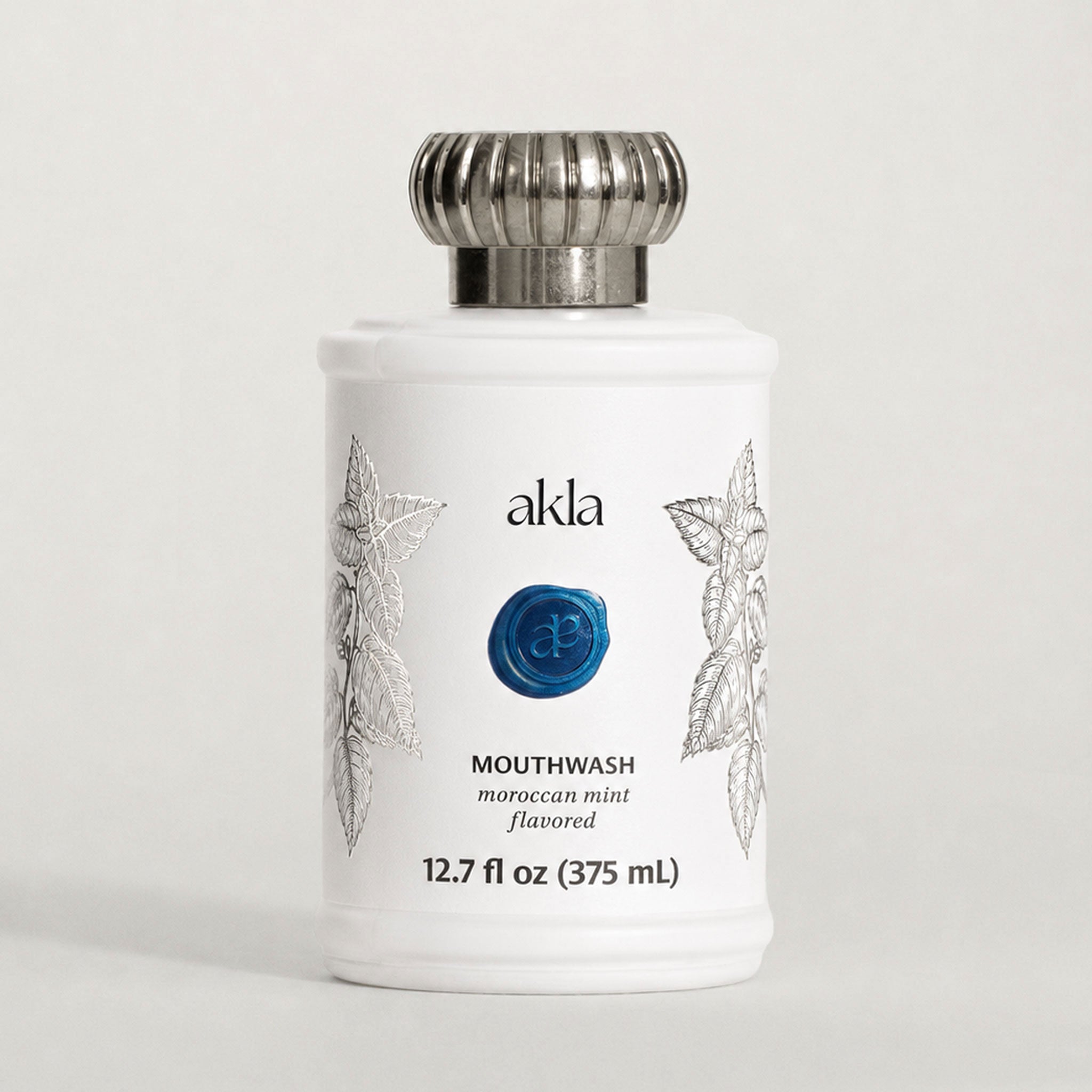 Akla alcohol-free mouthwash in a white glass bottle with brushed silver cap. Moroccan mint, fluoride-free, Swiss-made.