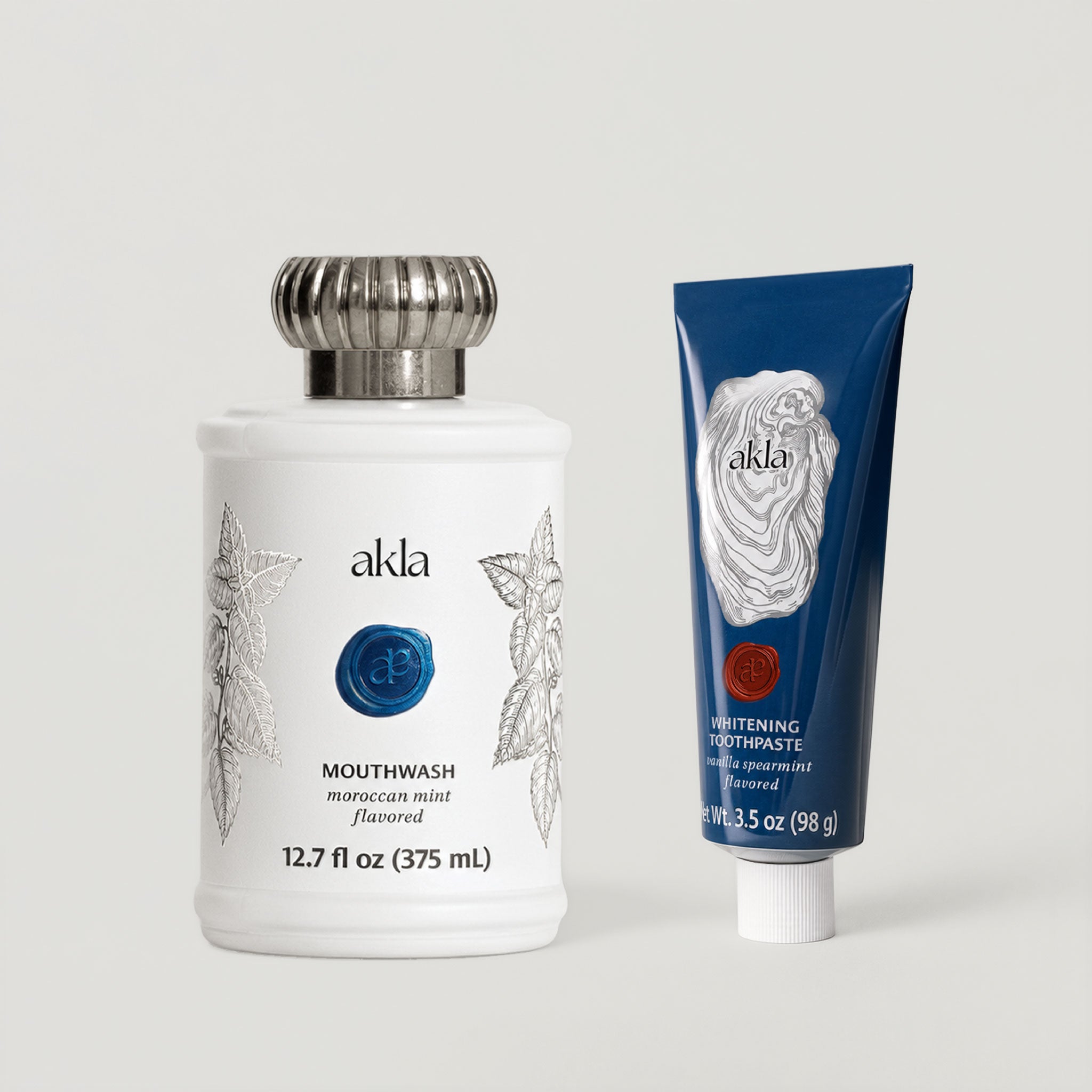 Akla Essentials Set shown at three-quarter angle with matte white glass mouthwash and navy aluminum toothpaste. Swiss-made oral care.