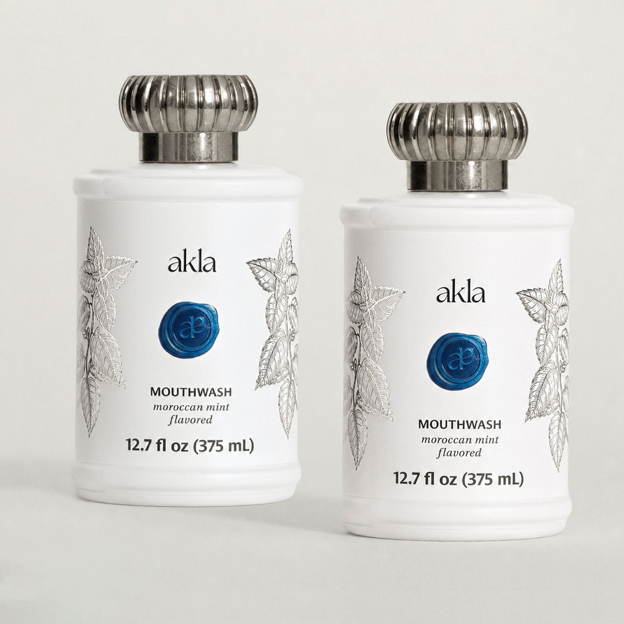 Akla Moroccan Mint Mouthwash duo in a matte white glass bottles with brushed silver caps. Alcohol-free botanical mouthwash, formulated in Switzerland.