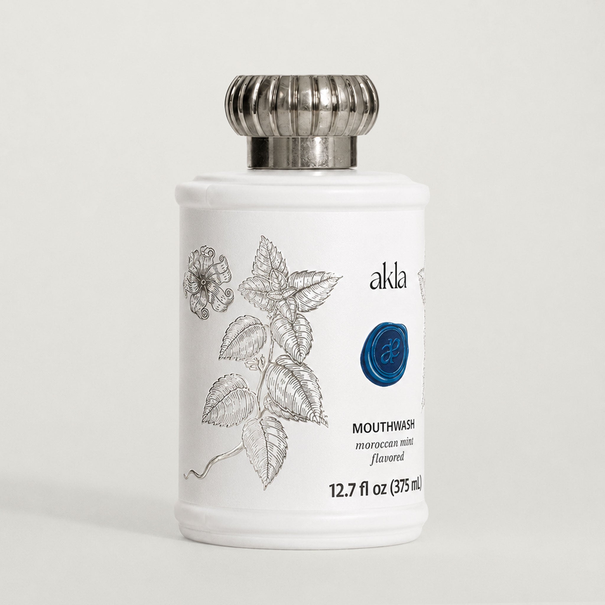 Akla Moroccan Mint Mouthwash shown at three-quarter angle in matte white glass with brushed silver cap. Swiss-made luxury oral care.