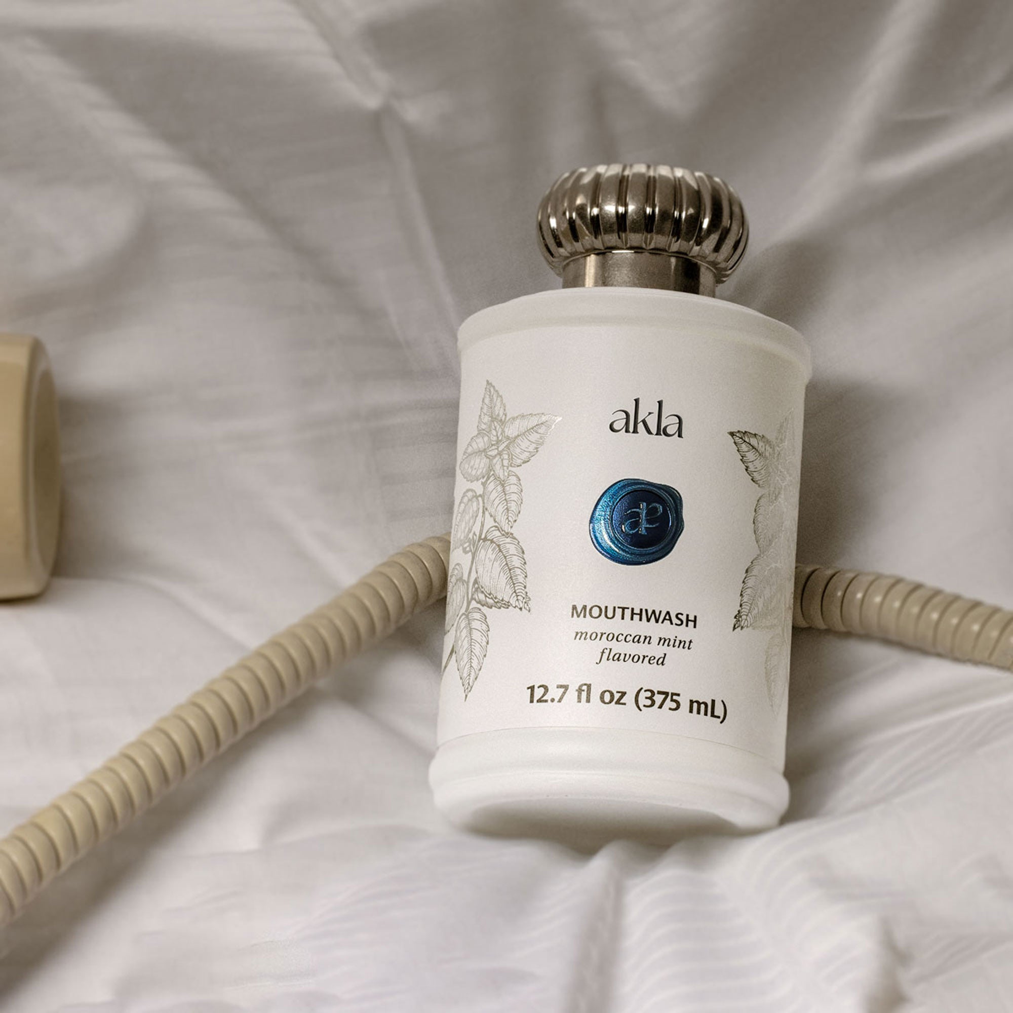 Akla mouthwash on hotel bed with phone cord – nighttime care.
