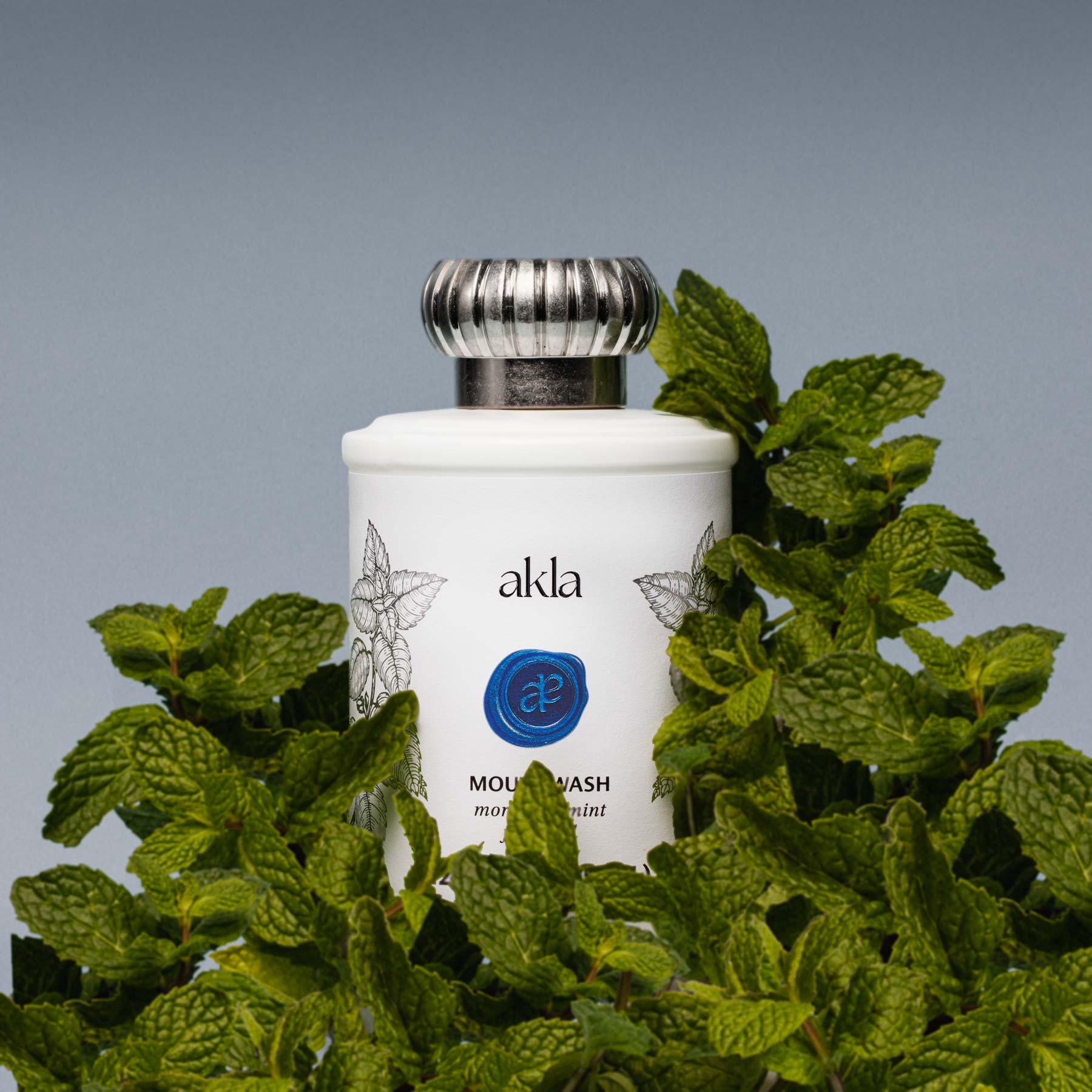 White glass bottle of Akla’s Moroccan Mint Mouthwash with mint botanical illustrations, representing freshness and fluoride-free oral care