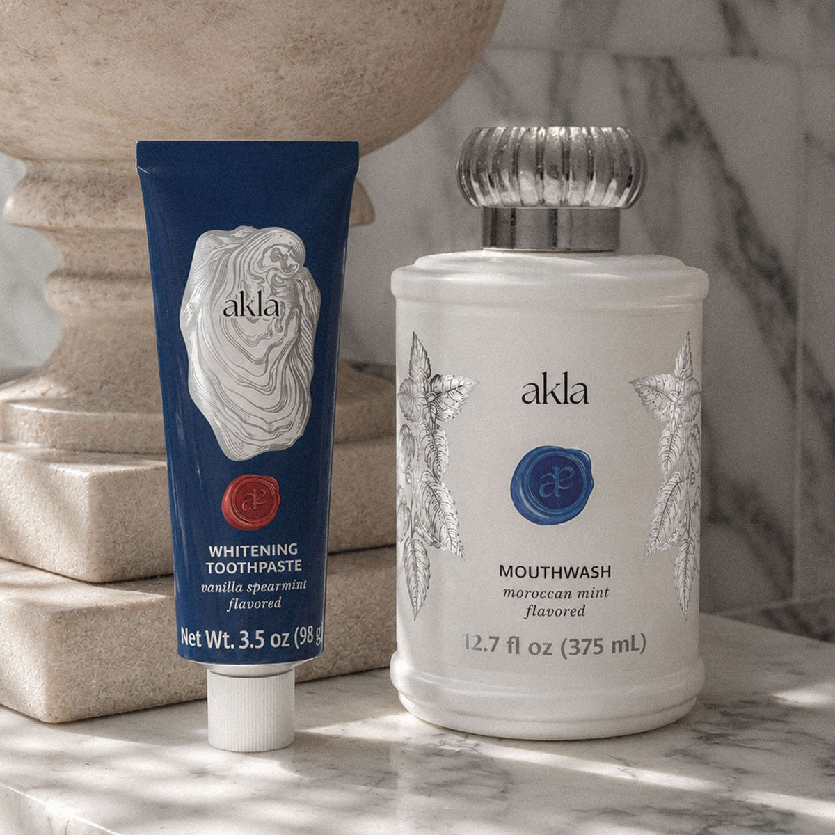Akla alcohol-free mouthwash in a white glass bottle and hydroxyapatite toothpaste in an alumimum tube displayed on a marble counter — Swiss-made luxury oral care.