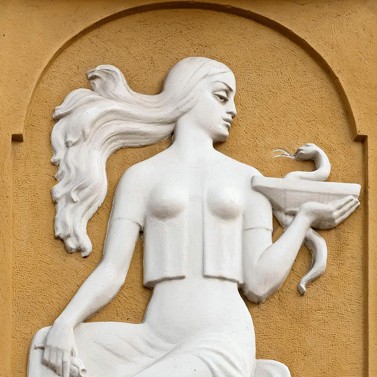 White stone statue relief of Hygieia, goddess of hygiene, set against an orange background symbolizing purity and ritual in Akla’s oral care philosophy.