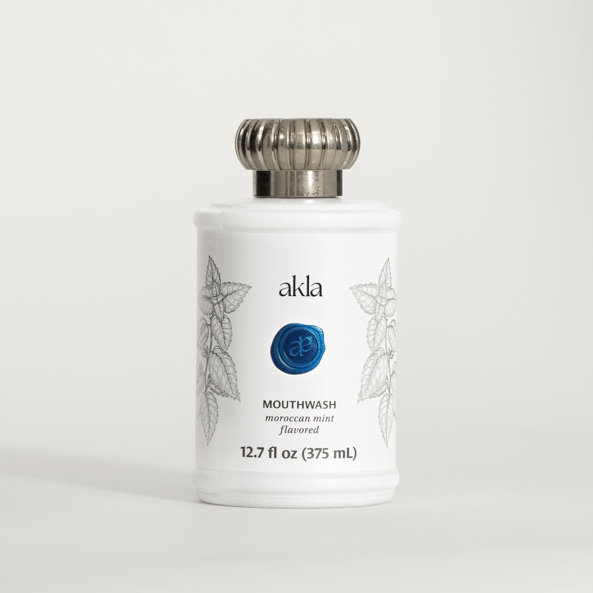 Akla Moroccan Mint Mouthwash – fluoride-free, alcohol-free mouthwash in white matte glass bottle with botanical engraving and blue embossed seal.