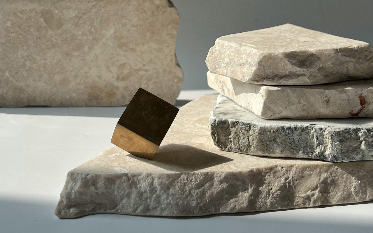 Stack of stone slabs with a metallic cube on top, against a neutral background