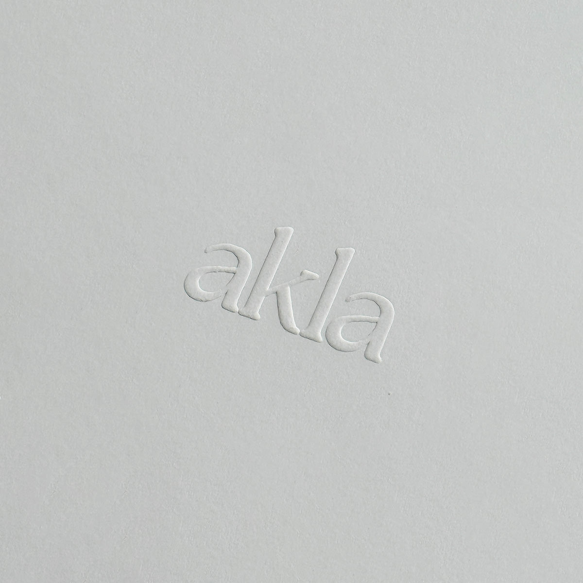 Embossed 'akla' logo on a light paper background.