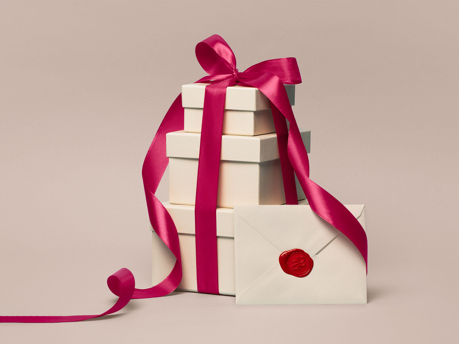 Stack of cream gift boxes tied with a fuchsia ribbon, next to an envelope with a Akla's wax seal monogram.