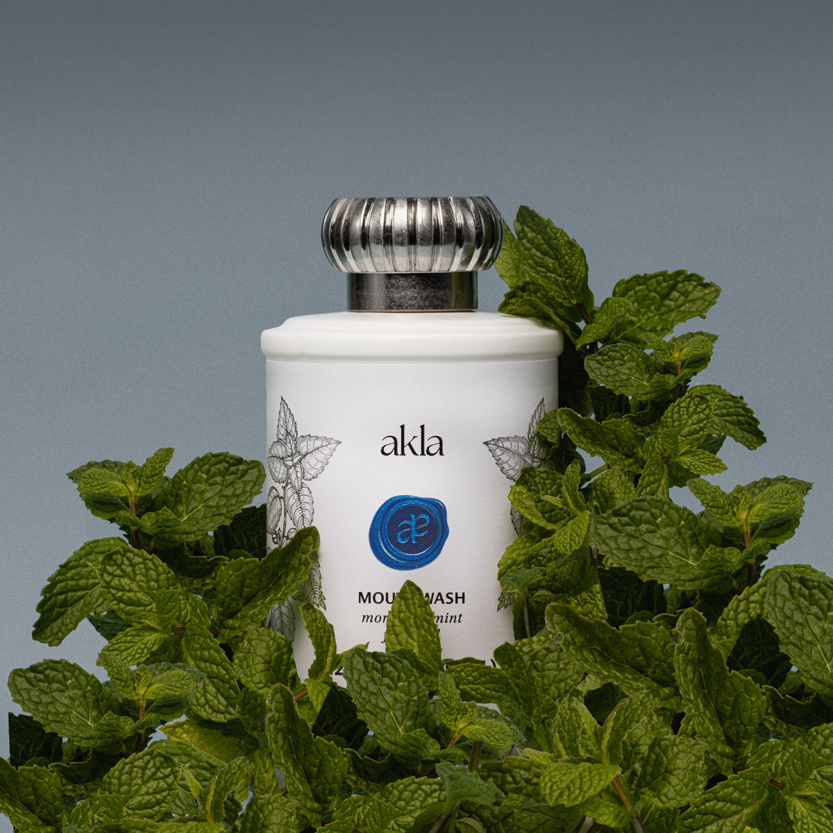 White glass bottle of Akla’s Moroccan Mint Mouthwash with mint botanical illustrations, representing freshness and fluoride-free oral care