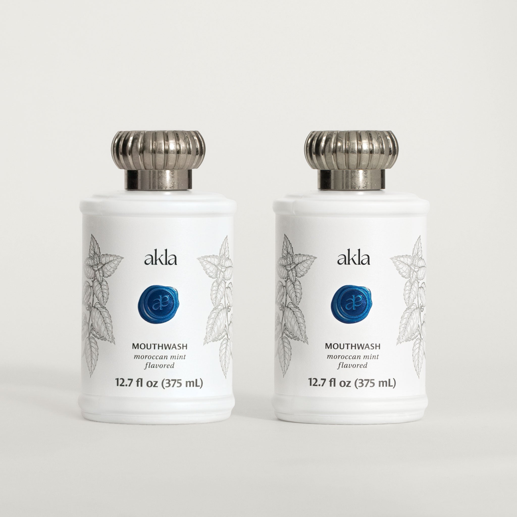 Akla Moroccan Mint Mouthwash Duo — two fluoride-free, alcohol-free rinses in white matte glass bottles with custom metal caps. Swiss-made.