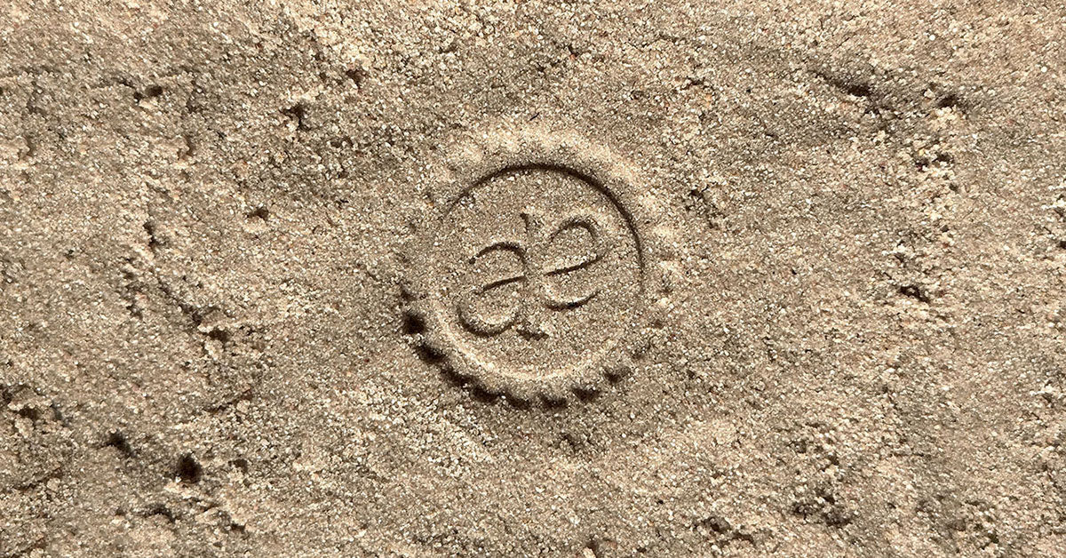 Akla monogram seal pressed into sand, representing luxury fluoride-free toothpaste design and timeless beauty in oral wellness.