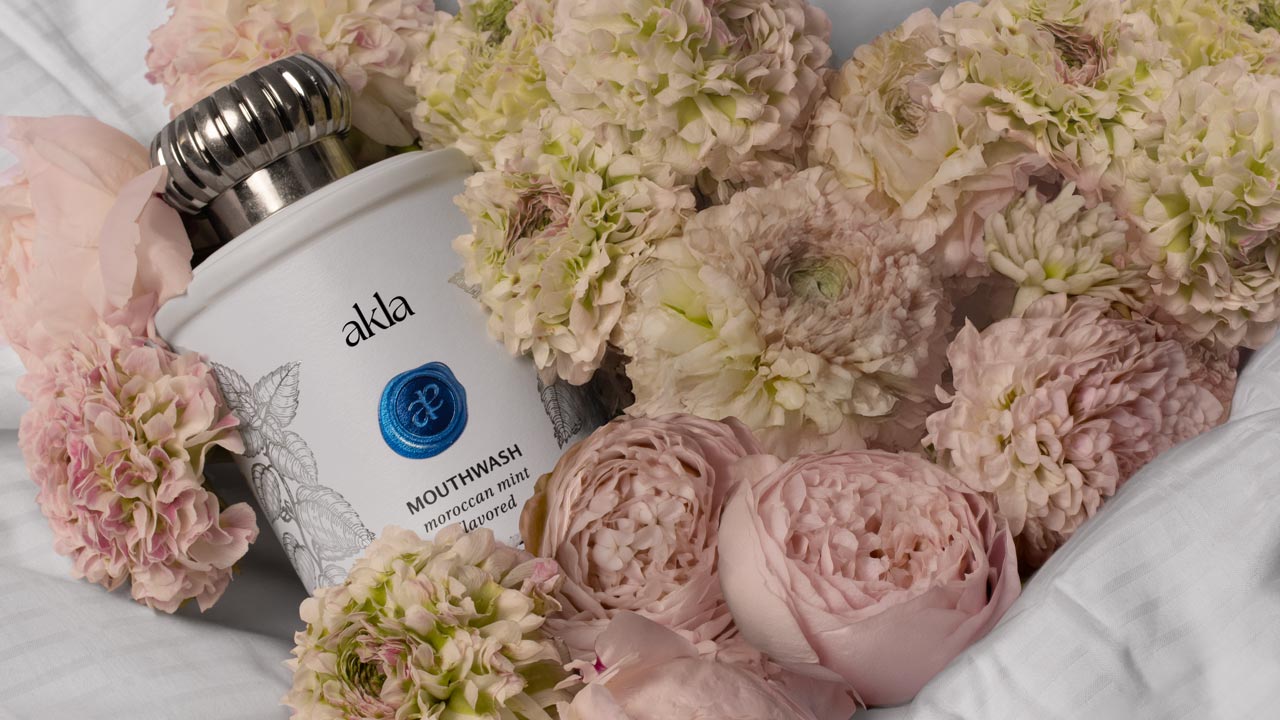 Swiss-made alcohol-free and fluoride-free Moroccan Mint mouthwash by Akla surrounded by soft florals, representing luxury oral care.