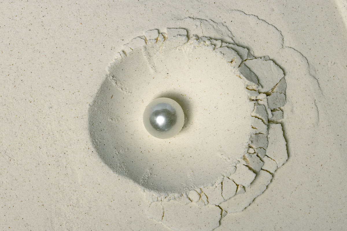 Close-up composition of finely milled pearl powder encircling a single luminous pearl, illustrating the transformation of natural minerals into refined oral care ingredients.