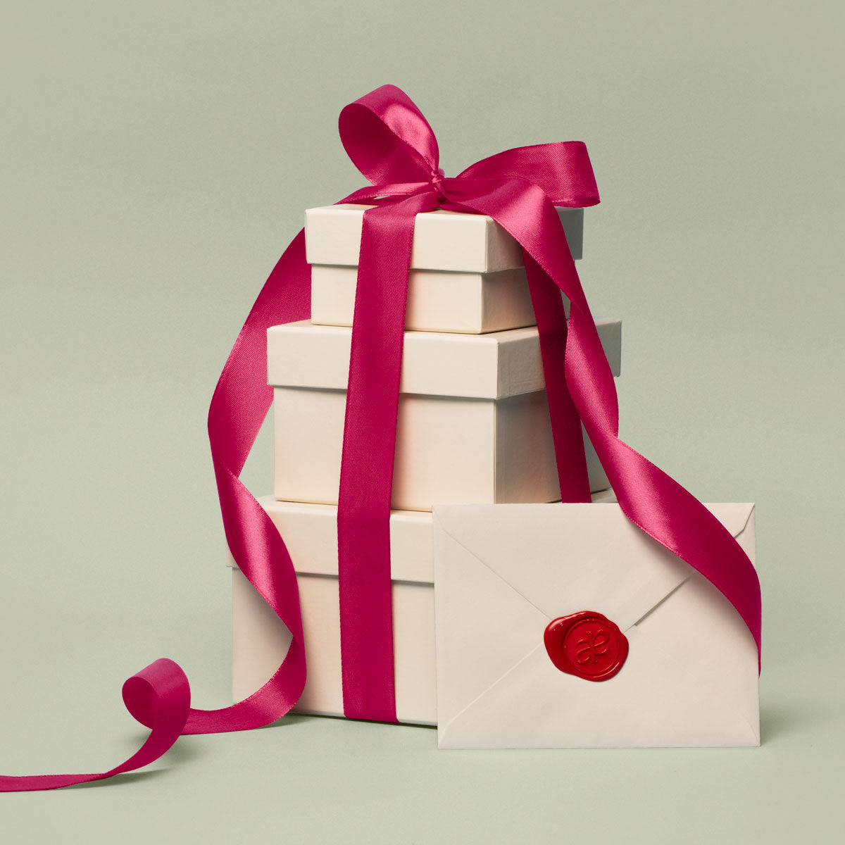 Stack of gift boxes with a pink ribbon and a letter with a red Akla monogram wax seal on a light green background.
